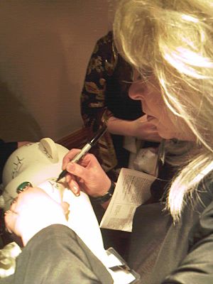 A woman with blonde hair using a sharpie to sign something.