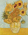 A ceramic vase with sunflowers on a yellow surface against a pale blue background.