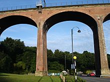 A large railway viaduct made from red bricks, topped by railings and electric pylons