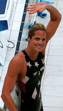 Smiling Torres in navy blue bathing suit with white stars, waving to crowd
