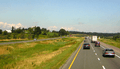 A four-lane divided highway among short hills travels into the background and curves to the right. The two divided halves are separated by a depressed swampy median.