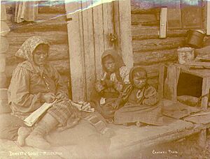 Indian woman with two children fashioning hide artifacts outside of cabin, Moosehide, Yukon Territory, ca 1900 (MEED 90)