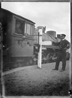 Changing the tablet at Horopito Railway Station, with an "X" class locomotive passing. ATLIB 289748