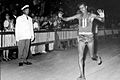 Abebe crossing the finish line, barefoot with hands raised, an Italian official in the background with a crowd of spectators behind a fence