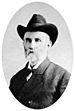 Head and shoulders of a white man with a graying beard, wearing a dark cowboy hat, suit coat, and bowtie.
