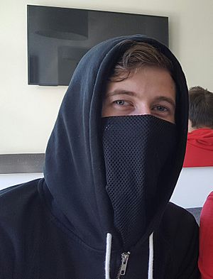 A young man in a dark blue hoodie looks at the camera with his lower face covered by an opaque mesh material of the same color.