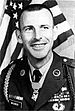 A black and white image of Morris from the chest up in his military dress uniform with ribbons. He has no hat and there is an American flag in the background.