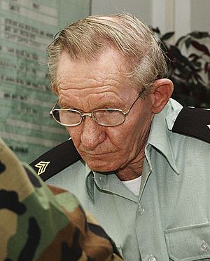 A candid photo of a white man in a woodland-camoflauge US Army uniform; he is looking downward and to the left of the camera