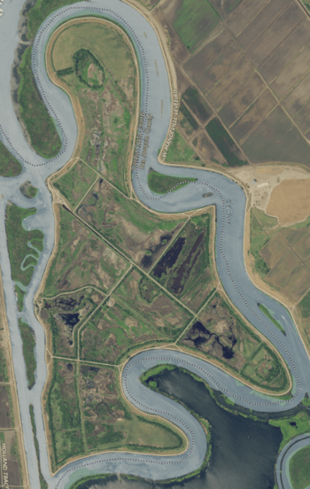 An aerial photograph of a flat island covered in farmland and surrounded by undulating rivers, causing its overall shape to be whorly.