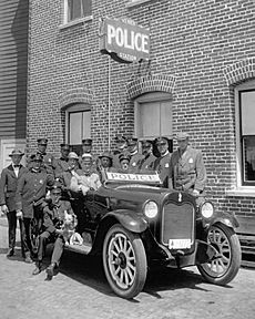 Fifteen uniformed policemen gather around a police car adjacent to the Venice Police Station, ca.1920