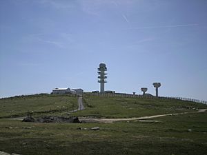 Three radio towers and several buildings on top of a mountain