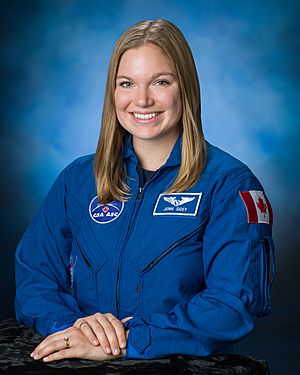 Jenni Sidey-Gibbons, wearing her blue Canadian Space Agency uniform bearing the flag of Canada, smiles at the camera, her hands folded.