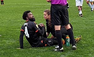 Dominic Samuel sitting on the pitch being attended by medical staff