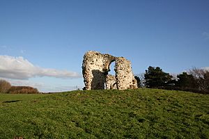 A white archway and portion of wall stand isolated in a grassy field under a blue sky