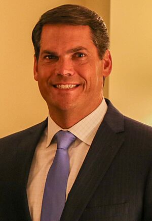 Portrait of Geoff Duncan in blue dress shirt with sleeves rolled up and red necktie, arms folded, in front of a U.S. flag.