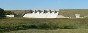 Concrete structure in grass-covered earthen dam; six floodgates