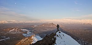 An ISAF member stands on top of a hill watching a snow-covered mountain range in Kabul province