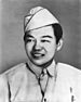 Head and shoulders of a smiling young man wearing a garrison cap and a shirt and tie, the bottom of the tie tucked into the shirt between the buttons.