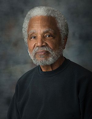 Formal/Professional photo of Ernie Chambers while he was serving as Nebraska senator for District 11. An older black man with white hair, in a black shirt with a gray background.