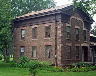 A two-story brown house made of small stones in rows. There are two small satellite dishes on top.