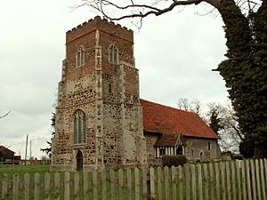 A church seen from the southwest.  The body of the church and the lower part of the tower are in stone, the upper part of the tower is red brick, the south porch is timber-framed, and the roof is covered in red tiles