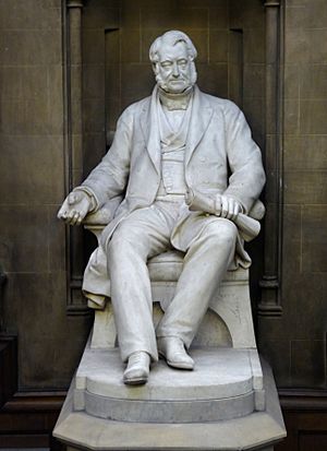 A white statue of a seated middle-aged man in mid-19th Century clothing, holding rolled plans in his left hand