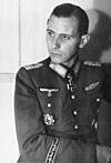 Black-and-white portrait of a man in semi profile wearing a military uniform with various military decorations, his dark hair is parted and combed back.