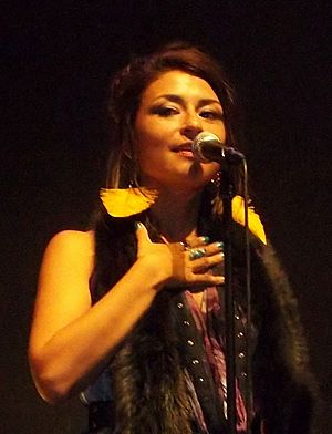 blurry picture of Elisapie onstage in front of a microphone, with right hand help up to her chest