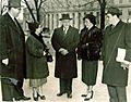 Five persons stand in heavy overcoats in front of an imposing federal building