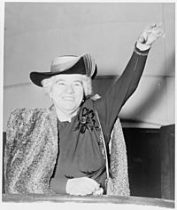 Photo of Elizabeth Kenny 1950, with short white hair, smiling and waving