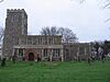 A rubble-stone church with a slate roof. On the west end is a castellated tower, with lower nave and chancel to the east. A red brick porch fronts the building