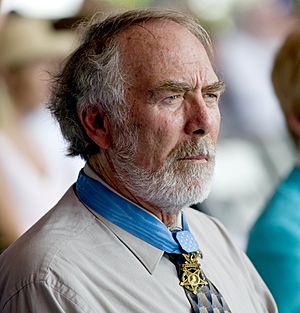 Profile of a white man with a full, gray beard wearing a star-shaped medal from a blue ribbon around his neck.