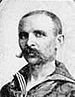 Head of a white man with a very wide handlebar mustache and closely cropped hair wearing a sailor suit.