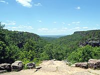 View into a river valley from a rock outcropping, with green forest below and blue sky above