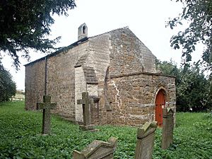 A small, very plain stone church seen from an angle, consisting of a single cell with a porch at the west end, a bellcote at the far end, and no visible windows