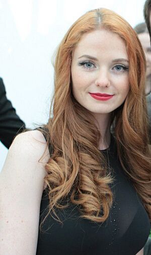close-up of Lena Katina wearing a sheer, black, sleeveless top revealing a black bra, smiling directly at camera