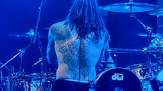 A man singing, his back tattoo visible