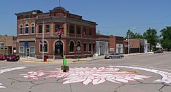 One- and two-story brick buildings seen across a street intersection; crowned eagle painted on the pavement, filling most of the intersection