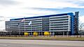 A wide rectilinear six-story blue-and-white building with the American, Canadian and Mexican flags flying in front, seen from a nearby roadway, under a cloudy sky