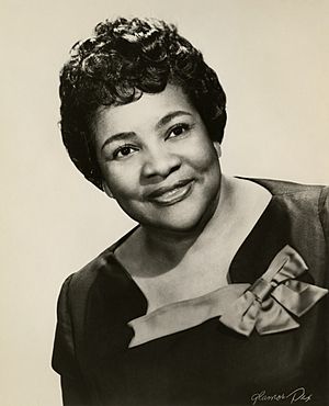 Photograph of a short-haired African American woman in a dark dress with a large bow on the neckline.