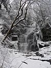 A very tall waterfall in the midst of snow-covered rocks and trees