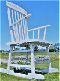 A large wooden rocking chair painted white against a blue sky and grass