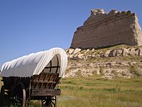 Covered wagon in front of large tan bluff