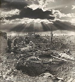 A sunburst through the clouds is shown against a landscape of destroyed land with a shell hole in the foreground.