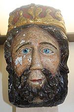A crudely carved and brightly painted image of a king with a thick beard, bright blue eye and crown.