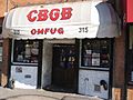 The front of the music club CBGB is shown. An awning has the letters CBGB painted on it. Below the name are the letters "OMFUG".