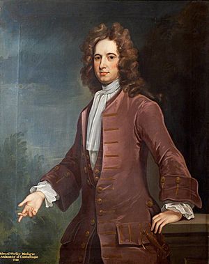 Standing half-length painted portrait of Edward Wortley Montagu wearing a coat, with left hand on a table