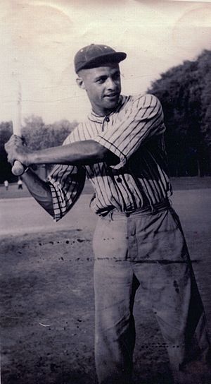 A man wearing a cap, standing with a baseball bat raised to shoulder level