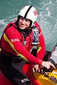 RNLI crewman seated in small inflatable, wearing helmet and bright red wetsuit.