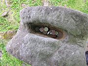Photo of the top of the bilateral statue, with an indentation filled with coins